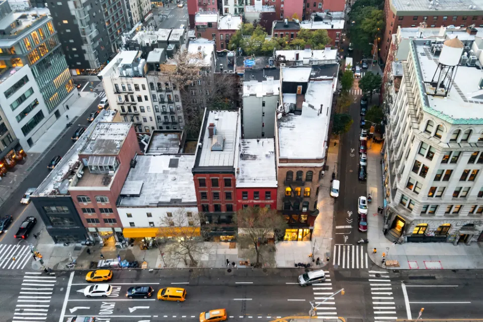A block of the Bowery in New York City seen from high above, with taxis and other cars passing on the street in front of the buildings.